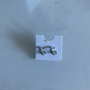 Silverfärgade örhängen - Snygga och stilrena silverfärgade örhängen i en elegant, böjd design. Perfekta för att ge en touch av elegans till vilken outfit som helst. Lätta att matcha med andra smycken.