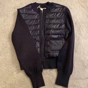 Mörkblå Y lightweight rib jacka från Gina Tricot - Snygg mörkblå Y lightweight rib jacka från Gina Tricot med quiltade detaljer och dragkedja framtill. Jackan har långa ärmar och en praktisk ficka på framsidan. Perfekt för en stilren look!