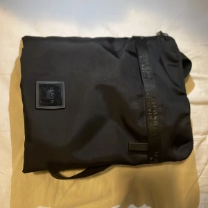 Svart axelväska med dragkedja - Snygg och praktisk svart axelväska med dragkedja. Tillverkad i slitstarkt syntetmaterial och har en justerbar axelrem. Perfekt för att bära med sig det nödvändigaste på ett stilrent sätt.