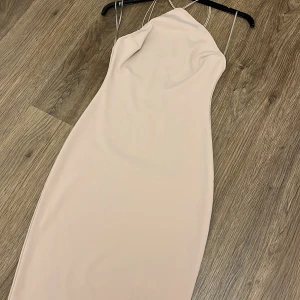 Champagnefärgad axelbandslös klänning - Elegant champagnefärgad klänning med smala axelband och en figurnära passform. Perfekt för en stilren look.