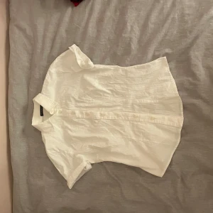 Vit kortärmad skjorta från Brandy Melville - Säljer en stilren vit skjorta från Brandy Melville. Skjortan har korta ärmar och knappar framtill, perfekt för en avslappnad look. Passar bra till både jeans och kjol. alldrig använd. i deras onesize storlek som jag skulle gissa är allt från m till kanske xs men kontakta privat om ni vill se på