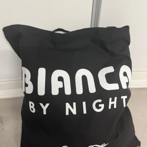 Bianca by Night påse - Stor och rymlig svart shoppingväska från Bianca by Night. Perfekt för att bära med sig allt man behöver under dagen. Väskan har ett enkelt och stilrent tryck på framsidan. Endast påsen ingår