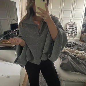Grå poncho med krage - Säljer en stilren grå poncho med krage och knappar framtill. Perfekt för lager-på-lager under kyliga dagar. Den har en lös passform och vida ärmar som ger en avslappnad look. Storlek S (brukar vanligtvis ha xs så funkar för både) 