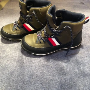 Gröna boots med snörning - Snygga gröna boots med snörning och detaljer i rött, vitt och blått. Perfekta för utomhusaktiviteter med robust sula för bra grepp. Stilren design med hög ankel och bekväm passform.