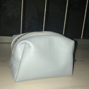 Ljusblå necessär med dragkedja - Söt och kompakt ljusblå necessär i syntetmaterial med dragkedja. Perfekt för att förvara smink eller småsaker när du är på språng. De jättesmå vita fläckarna är jättelätta att få bort och tas såklart bort innan paketet skickas. Frakt betalas av köpare. 