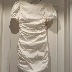 Vit klänning  - Säljer en stilren vit klänning med kort puffärm och en elegant öppen rygg med knytband. Klänningen har en åtsittande passform. Helt ny med prislapp kvar! Perfekt till studenten eller sommaren 💕