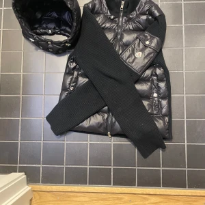 Svart pufferjacka från Moncler - Snygg svart pufferjacka från Moncler med quiltad design och dragkedja framtill. Jackan har långa ribbade ärmar och praktiska fickor med knappar. Perfekt för kyligare dagar.