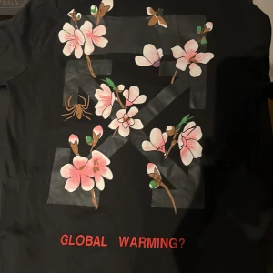 Svart t-shirt från Off-White - Snygg svart t-shirt från Off-White med tryck av blommor och texten 'GLOBAL WARMING?' i rött. T-shirten har korta ärmar och ett stilrent tryck på baksidan med texten 'OFF'. Perfekt för en trendig look. Ny pris 4000kr den är perfekt skick kom med förslag 