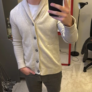 Beige kofta med knappar - Säljer en stilren beige kofta med knappar och en bred krage. Perfekt för lager-på-lager och passar till både vardag och mer uppklädda tillfällen. Koftan har långa ärmar och en mjuk, bekväm passform. Passar om du är ca 175cm. Skriv vid funderingar!