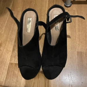 Svarta klackskor från Atmosphere - Snygga svarta klackskor från Atmosphere med öppen tå och justerbart spänne runt ankeln. Perfekta för en kväll ute eller en speciell tillställning. Storlek 37. Lite smutsiga men går att göra rent
