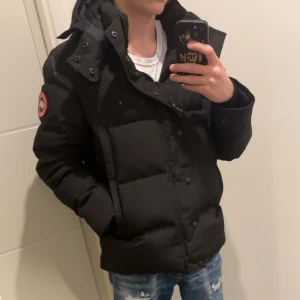 Canada goose jacks  - Säljer en svart jacka från Canada Goose med avtagbar huva och pälsdetalj. Jackan har en klassisk design med knappar och dragkedja framtill samt en broderad logotyp på ärmen. Namn på jackan Canada goose Wyndham 1:1k i storlek:M har endast haft den i några dagar  då ah köpt en pjs jacka och inte behöver denna mer (pris kan diskuteras) 