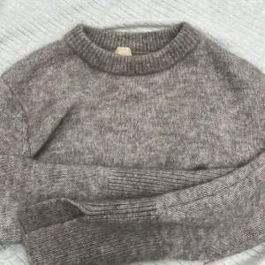 Grå mohair/ulltröja från H&M - Mysig grå tröja från H&M i en mjuk mohair- och ullblandning. Perfekt för kyliga dagar med sin klassiska design och ribbade detaljer vid hals, ärmslut och nederkant.