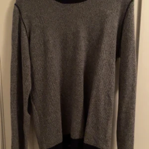 Grå tröja från Suit - Säljer en stilren grå tröja från Suit med svarta detaljer vid armbågarna. Tröjan har en rund hals och långa ärmar, perfekt för en avslappnad look. Passar bra till både jeans och chinos.