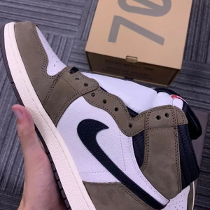 Nike Air Jordans i mocka och skinn - Säljer ett par snygga Nike Air Jordans i en cool kombination av brunt mocka och vitt skinn. Skorna har en svart swoosh och kommer med extra rosa skosnören för att ge en personlig touch. Perfekta för både vardag och fest!