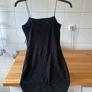 Svart klänning med tunna axelband - Säljer en stilren svart klänning med tunna axelband. Perfekt för en utekväll eller fest! Klänningen är i ett mjukt och bekvämt material som formar sig fint efter kroppen. Den är enkel men ändå elegant, vilket gör den lätt att matcha med olika accessoarer.