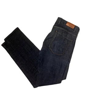 Mörkblå jeans från Oscar Jacobson - Säljer ett par snygga mörkblå jeans från Oscar Jacobson. De har en klassisk design med fem fickor och en knappgylf. Jeansen är i bra skick och har en stilren look som passar både till vardags och fest. Perfekta för höst och vinter!