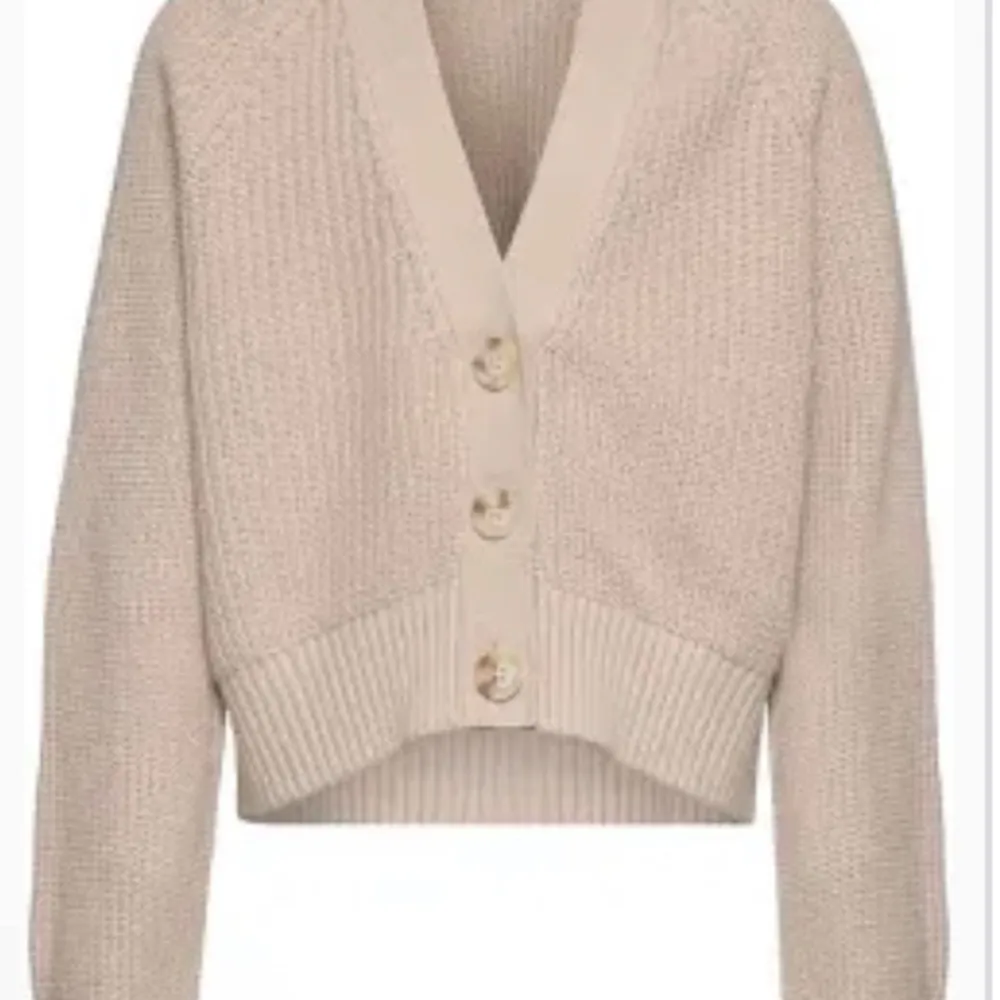 Säljer en superfin beige stickad kofta med stora knappar framtill. Den har en croppad stil och ribbade kanter som ger en snygg look. Perfekt för höst och vår när du vill ha något mysigt men ändå stilrent. Passar till både jeans och kjol!. Tröjor & Koftor.