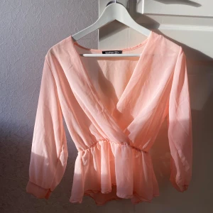 Persikofärgad blus från Boohoo - Säljer en söt persikofärgad blus från Boohoo. Den har en omlott-design med resår i midjan som ger en fin passform. Blusen har trekvartsärmar och är gjord i ett lätt och luftigt material, perfekt för vår och sommar. Passar både till vardags och fest!