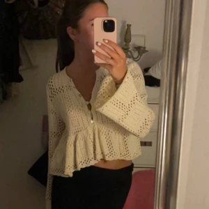 Beige spetskofta - Säljer en superfin beige spetskofta med volangdetaljer. Den är croppad och har långa ärmar, perfekt för en somrig look. Koftan har en v-ringad design och knappar framtill. Passar perfekt till både vardag och fest!