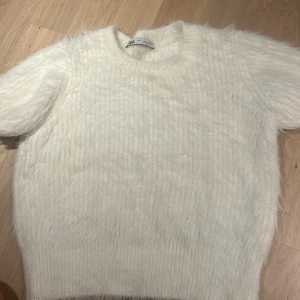 Vit fluffig tröja från Zara - Säljer en supermjuk och fluffig vit tröja från Zara. Den är perfekt för att hålla sig varm och stilren under kyliga dagar. Tröjan har en croppad passform och korta ärmar, vilket gör den både trendig och bekväm.  Passar xs! Då de är min storlek