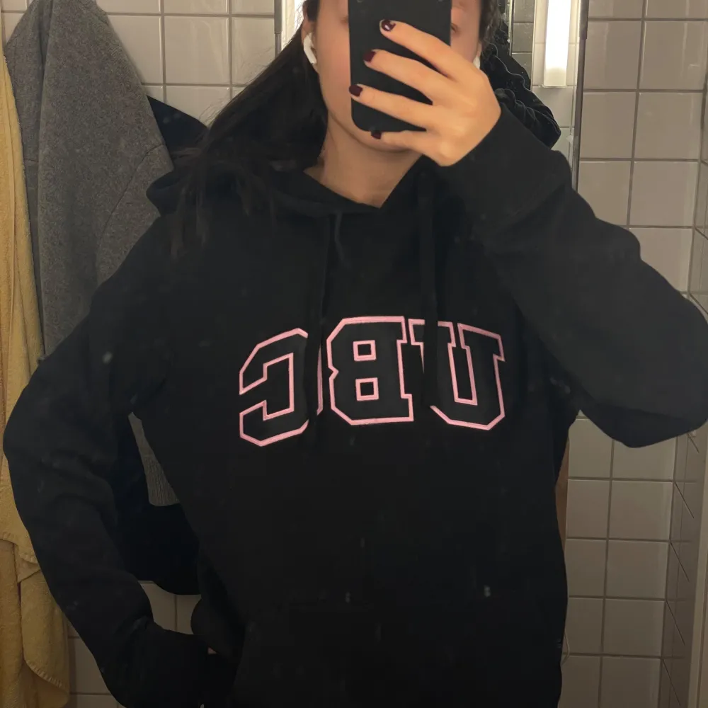 Säljer en svart hoodie med rosa UBC-tryck på bröstet. Den är superbekväm och perfekt för kalla dagar. Hoodien har en klassisk passform med en stor ficka fram och justerbar huva. Perfekt för både vardag och chill hemma. 🖤. Tröjor & Koftor.