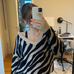 Zebramönstrad stickad tröja - Säljer en supermysig zebramönstrad stickad tröja i beige och svart. Den har en v-ringad design och långa ärmar, perfekt för höst och vinter. Tröjan är oversized och ger en avslappnad look. Perfekt för att mysa hemma eller en dag på stan!