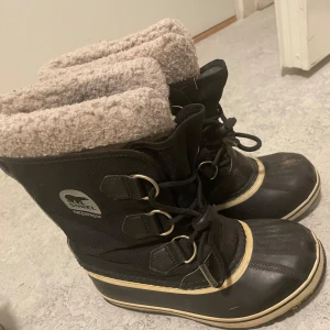 Svarta vinterstövlar från Sorel 33 - Säljer ett par svarta vinterstövlar från Sorel i bra skick i storlek 33. De har en varm och mysig pälsfodring som är tvättbara och snörning framtill. Perfekta för kalla vinterdagar med sitt robusta och vattentäta material. 