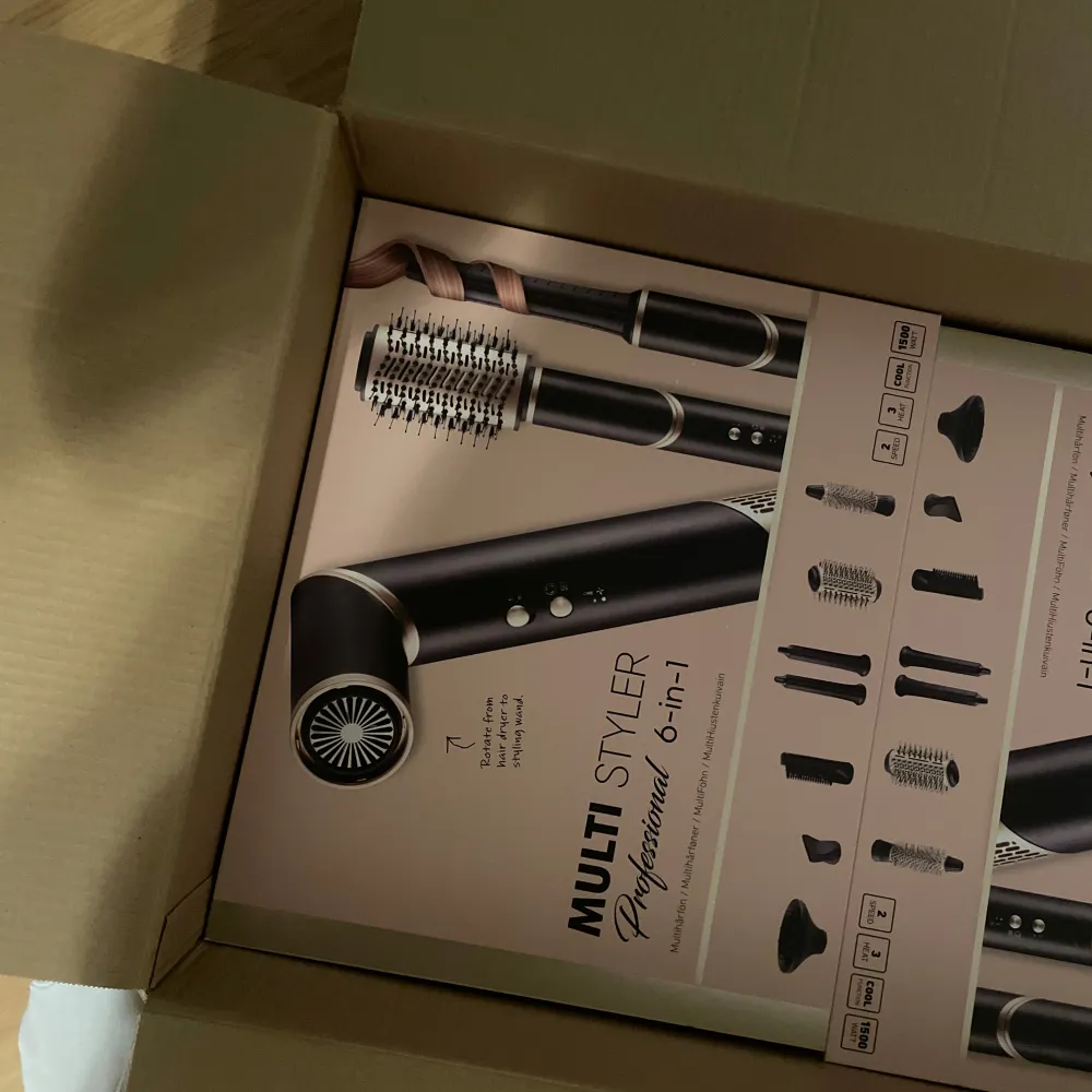 En Multi Styler Professional 6-in-1 hårstyler i svart och silver. Den har flera utbytbara tillbehör för olika stylingbehov, inklusive borstar och munstycken. Perfekt för att skapa olika frisyrer med en enda enhet.. Skönhet.