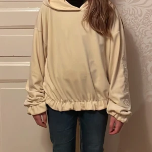 Beige hoodie i fleece - Mysig beige hoodie i fleece med oversized passform. Perfekt för kalla dagar med sin varma och sköna känsla. Den har långa ärmar och en stor huva för extra komfort. Passar perfekt till vardags eller mysiga hemmakvällar.