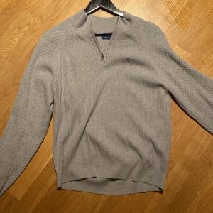 Grå ribbad tröja från GANT - Säljer en stilren grå ribbad tröja från GANT med dragkedja vid halsen. Perfekt för både höst och vinter. Tröjan har långa ärmar och ett broderat GANT-emblem på bröstet. Superbekväm och passar till alla tillfällen! Säljer den för riktigt bra pris då den bara hänger i garderoben samt är för liten. Storlek XS/ 170 cm. Ny pris: ca 1200. Mitt pris 250
