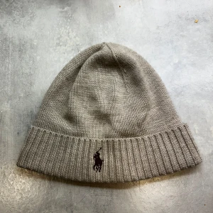  Polo Ralph Lauren mössa - Säljer en snygg beige mössa från Polo Ralph Lauren i merinoull. Perfekt för att hålla sig varm under höst och vinter. Mössan är i mycket bra skick och passar de flesta tack vare one size-storleken. Säljer den då jag ej använder den och den är knappt använd (använd max 2 gånger)