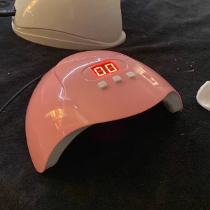 Helt oanvänd uv lampa - En rosa LED-lampa för naglar med digital display och tre knappar för tidsinställning. Perfekt för att härda gelnagellack snabbt och effektivt. Den har en kupolformad design och flera LED-lampor inuti för jämn belysning.