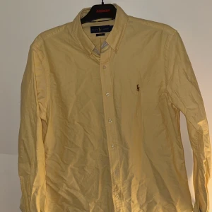 Gul skjorta från Ralph Lauren - Säljer en snygg gul skjorta från Ralph Lauren i slim fit. Skjortan är långärmad och har klassiska knappar framtill. Perfekt för både vardag och fest! 🟡