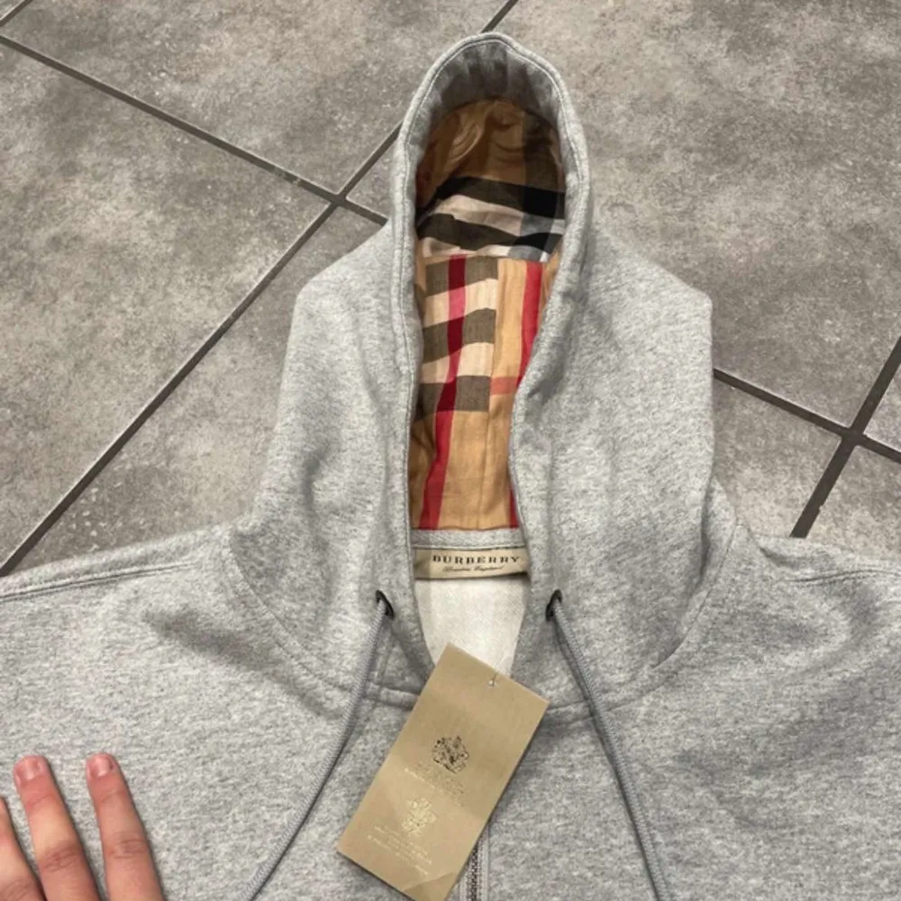 Säljer en snygg grå hoodie från Burberry i nytt skick. Den har en klassisk dragkedja och den ikoniska Burberry-rutiga insidan av huvan. Perfekt för höst och vår, och passar både till vardags och lite mer uppklädda tillfällen. Storleken är normal och materialet känns mjukt och bekvämt. Tröjan har en defekt och de är att dragkedjan är lite trög men annars är den i fint skick!ops(pirslappen har jag råkat slänga) storlek xs är väldigt svårt o få tag därför är priset som det är.. Tröjor & Koftor.