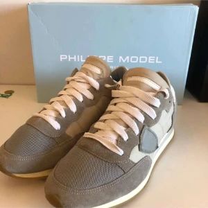 Grå sneakers från Philippe Model - Säljer ett par snygga grå sneakers från Philippe Model i mycket bra skick. Skorna har en stilren design med snörning och är tillverkade i en kombination av mocka och syntetmaterial. Perfekta för både vardag och festliga tillfällen!