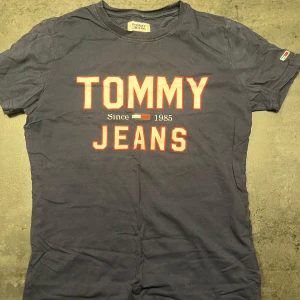 Mörkblå t-shirt från Tommy Jeans - Säljer en snygg mörkblå t-shirt från Tommy Jeans med stort tryck på framsidan. Den är kortärmad och i bra skick, perfekt för vardagsbruk eller en avslappnad dag ute. Materialet känns mjukt och skönt mot huden. Passar perfekt till jeans eller shorts! Nypris 300:-