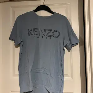 Säljer en snygg ljusblå t-shirt från Kenzo. Perfekt för en casual look och passar bra till både jeans och shorts. T-shirten är i bra skick och har en normal passform. Perfekt för vår och sommar!