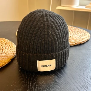 Dondup mössa - Säljer en snygg svart ribbad mössa från Dondup. Den är i one size och tillverkad i Italien. Perfekt för att hålla sig varm nu till vintern. Mössan har en vit etikett med märkesnamnet framtill. Nypris 860-900.