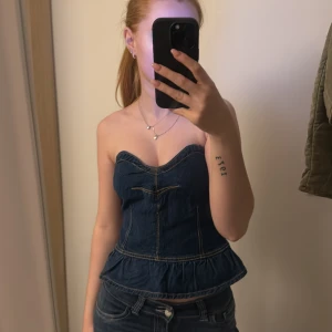 Jeansfärgad korsett - Snygg jeansfärgad korsett i denimstil med en peplumdetalj längst ner. Den är axelbandslös och har en dragkedja i ryggen för enkel på- och avtagning. Perfekt för en utekväll eller fest! Helt oanvänd !