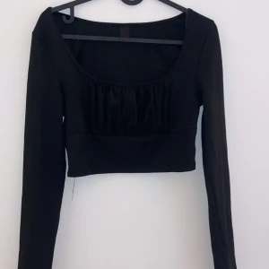 Svart långärmad topp - Snygg svart långärmad topp med en croppad passform. Den har en fin rynkad detalj framtill som ger en extra touch. Perfekt för både vardag och fest! 🖤