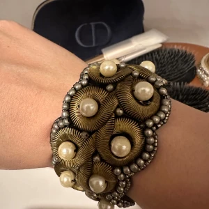 Unikt armband med pärlor och metall - Säljer ett unikt ställbart armband med en fin design av metall och stora pärlor. Armbandet har en vintagekänsla med sina detaljerade mönster och pärlor som ger en lyxig touch. Perfekt för att piffa upp vilken outfit som helst! 🖤 I nyskick! Köpt på Raglady, nypris 800kr