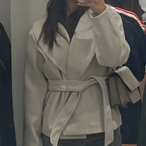 Beige kappa med bälte - Säljer en superfin beige kappa i ull med bälte i midjan. Perfekt för höst och vår! Den har en elegant omlott-design och långa ärmar. Kappan är i bra skick och passar till både vardag och fest. 🧥✨