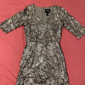 Glittrig klänning från Rebecca Stellas kollektion från Nelly - Säljer en superfin glittrig klänning från Rebecca Stella för Nelly. Den har en v-ringad design med trekvartsärm och är täckt av paljetter i silver. Perfekt för festliga tillfällen! Klänningen har en dragkedja i ryggen för enkel påklädning. Den har endast används 1 gång och är perfekt för Nyår eller Jul! Priset är alltid diskuterbart!