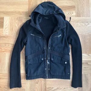 Svart cardigan jacka från Ralph Lauren - Säljer en snygg, sällsynt, black lable Ralph Lauren cardigan, jacka i storlek S. Jackans front panel och luva är i nylon medans back panel och ärmarna är i stickat merino wool. Den har dragkedja framtill och flera praktiska fickor. Köp second hand. Har täcken på användning, vilket syns på bilden och dragkedjan är lite knepig men fungerar.