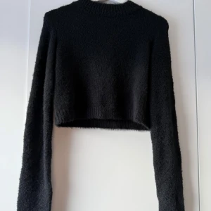 Svart croppad tröja från NA-KD - Säljer en supermjuk och stilren svart croppad tröja från . Perfekt för höst och vinter med sin varma och gosiga känsla. Tröjan har långa ärmar och en ribbad kant vid ärmslut och nederkant. Passar perfekt till både jeans och kjol! Passar MER strl XS