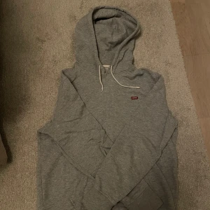 Levis hoodie - Säljer en snygg och bekväm grå hoodie från Levis. Den har en klassisk design med en liten röd Levis logga på bröstet. Perfekt för en avslappnad stil och passar till det mesta. Huvan har dragsko och tröjan är i mjukt material. Skriv vid minsta lilla fundering✍️😀✅