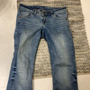 Blå jeans från H&M Divided - Säljer ett par snygga blå lågmidja jeans från H&M Divided i storlek 34. De har en klassisk femficksdesign med en knapp och dragkedja framtill. Jeansen är i bra skick 