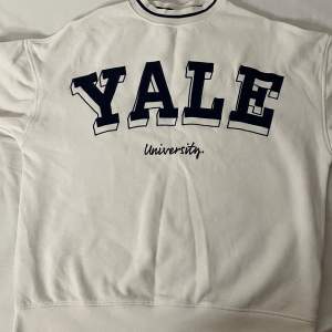 Säljer en vit sweatshirt med stort Yale University-tryck på framsidan och siffran 19 på ärmen. Perfekt för en avslappnad stil eller för att visa ditt stöd för Yale! Tröjan har en normal passform och är gjord i mjukt bomullsmaterial.