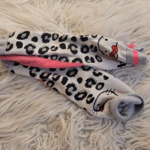 Hello Kitty strumpor med leopardmönster - Säljer ett par supergulliga Hello Kitty strumpor med leopardmönster i svart och grått. De har en söt Hello Kitty-design med rosa detaljer och är perfekta för att liva upp vilken outfit som helst. Strumporna är i bomull och i bra skick. Perfekta för alla Hello Kitty-fans! 🐱💖