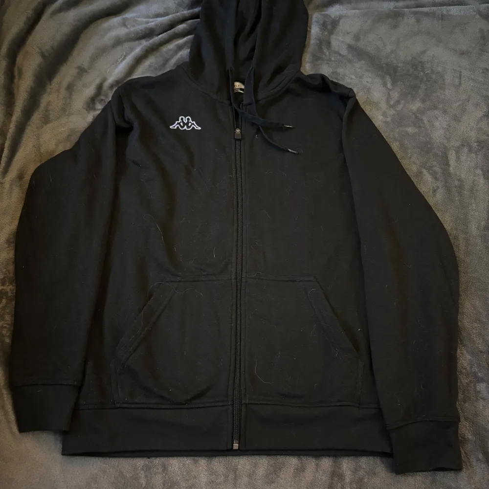 Säljer en svart hoodie från Kappa i storlek medium men är mer som S. Den har en dragkedja framtill och en klassisk Kappa-logga på bröstet. Perfekt för höst och vinter, med en skön passform och huva för extra värme. Perfekt för vardagsbruk eller chill dagar hemma.. Tröjor & Koftor.